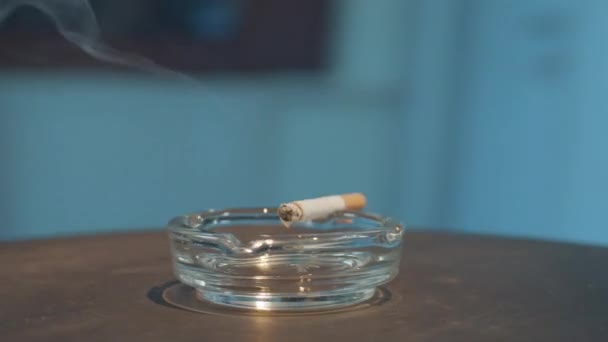 Rotation rapprochée du cendrier en verre avec cigarette brûlante placée sur son bord .