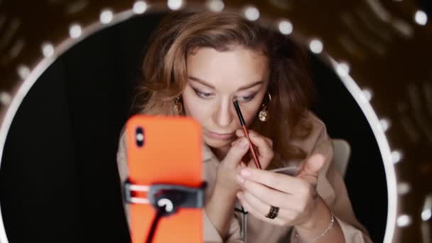 Caucásico mujer maquillaje artista se aplica sombra de ojos sentado en frente de la luz del anillo — Vídeo de stock