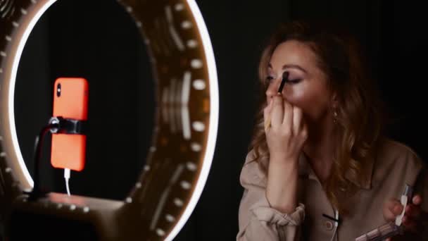 Όμορφη γυναίκα makeup artist εφαρμόζει σκιές ματιών κάθεται μπροστά από το φως δαχτυλίδι — Αρχείο Βίντεο