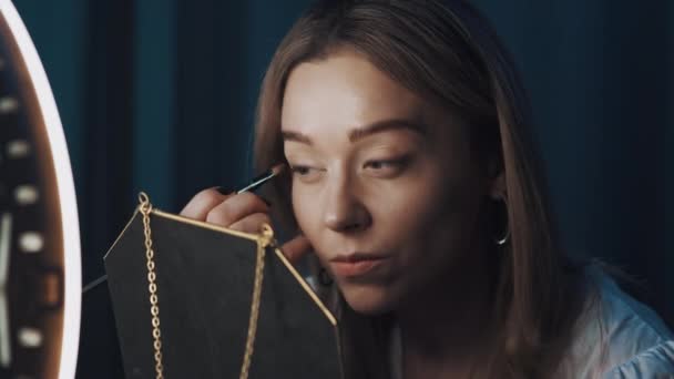 Woman fashion blogger uses eyeliner holding mirror in front of ring light. — Stock Video