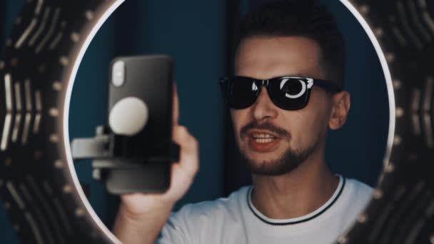 Aktive Brünette Mann Videoblogger mit Sonnenbrille spricht vor Ringlicht. — Stockvideo