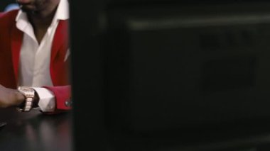 Sakallı, kel, Afro-Amerikan iş adamı, kırmızı takım elbiseli, beyaz gömlekli, şık gözlükleri olan, elinde akıllı telefon kullanan, karanlıkta oturan, klasik mavi renkli.