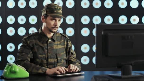 身穿迷彩服 头戴帽子 留着胡子的军人男子 拿着电脑坐在办公桌前 键入键盘 接听着绿色老式电话 然后站起身来离去 — 图库视频影像