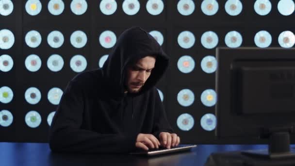 身穿黑色帽衫 面容忧心忡忡的高加索成熟男子电脑黑客坐在科技室里 积极地在键盘上打字 用蓝色经典灯光凝视着黑暗房间里的展品 — 图库视频影像