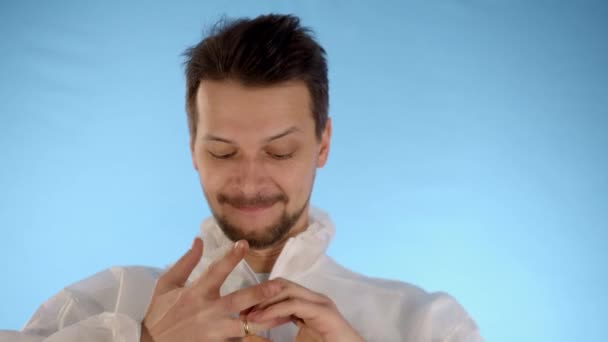 白胡子男子身穿蓝色背景的白色防护服 试图摘下订婚戒指 舔着手指 — 图库视频影像