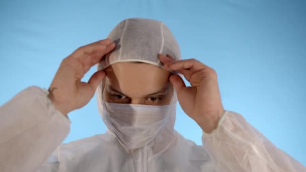 파란색 배경에 방호복을 수염을 남자가 후드에 의료용 마스크를 재킷의 지퍼를 — 비디오