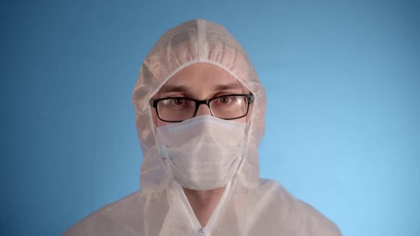 白人男性で白い保護スーツ 医療用マスク 青の背景にゴム手袋は 赤い液体 おもちゃのウイルスと手のテストチューブを保持し ウイルス感染プロセスを実証 — ストック動画