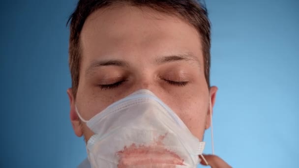 파란색 배경에 남자가 얼굴에 피묻은 의료용 마스크를 있습니다 — 비디오