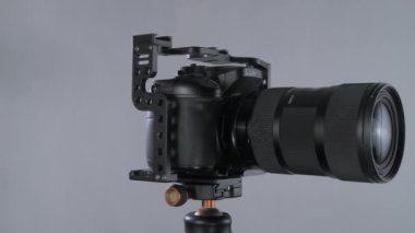Kafesteki aynasız kamera metabon hızlandırıcılı ve yakınlaştırmalı lens sigması tripodda dönüyor, fındık grisi arka planda izole edilmiş yakın plan..