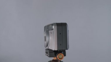 Stüdyodaki fındık grisi arka planda tripodda 360 derece dönen küçük çizilmiş eski bir fotoğraf makinesi..