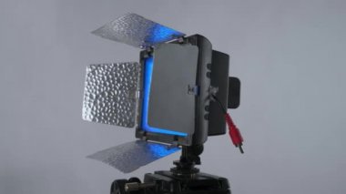 NPF bataryalarından çalışan mavi filtreli profesyonel taşınabilir video ışık paneli, stüdyodaki fındık grisi arka planda 360 derece dönüyor..