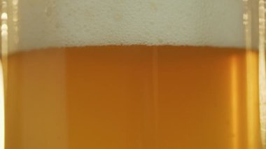 Güneş filtresiz biranın içinden parlıyor bardağa dökülüyor, kabarcıklar yükseliyor ve köpük yukarı çıkıyor yakın çekim için..