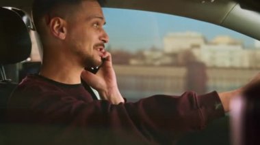 Çekici kısa saçlı beyaz adam araba kullanıyor ve akıllı bir telefonla konuşuyor..