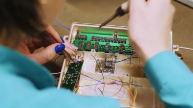Boyanmış çivileri olan kadın bir laboratuvar teknisyeni mikro devreyi onarmak için lehim makinesi kullanıyor..