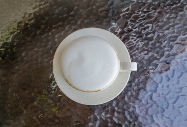 Beyaz fincan kahve, latte cam masa üzerinde güzel süt köpüğü ile kapatmak.