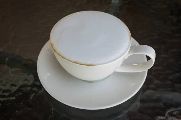Feche a xícara branca de café, latte com espuma de leite bonita na mesa de vidro . — Fotografia de Stock