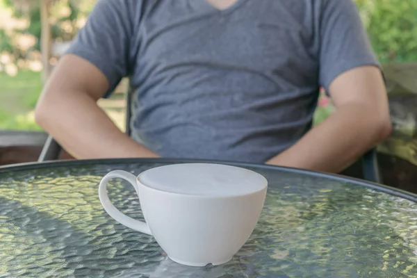 Mann und heiße Tasse Kaffee mit mehr Milchschaum auf dem Glastisch. Liebendes Kaffee-Konzept. — Stockfoto