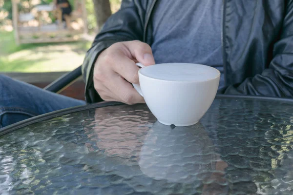 Man met warme kop koffie met meer melk schuim op de glazen tafel. Liefdevolle koffie concept. — Stockfoto