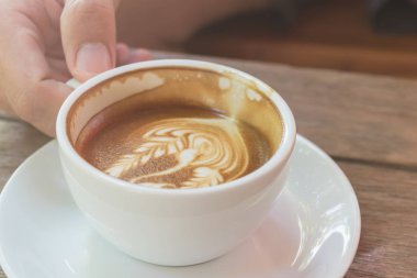 Beyaz fincan kahve, latte güzel latte art ahşap masa tarih ile kapatmak.