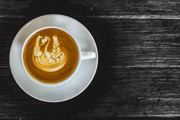 Kahve, latte ile güzel latte sanat siyah ahşap zemin üzerine beyaz fincan kapatmak.