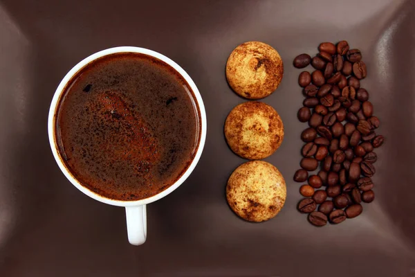 Чашка черного кофе с печеньем и бобами на темной тарелке — стоковое фото