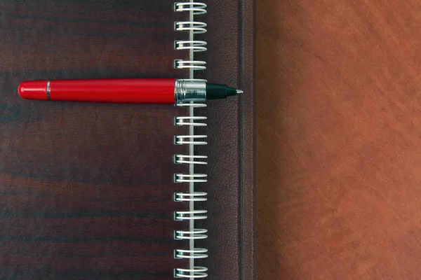notebook and a red pen lying on wooden desk