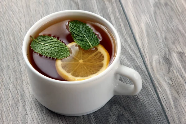 Cangkir teh putih dengan lemon dan mint di atas meja kayu — Stok Foto