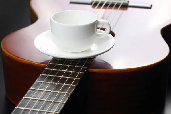 empty white cup lying on the acoustic guitar