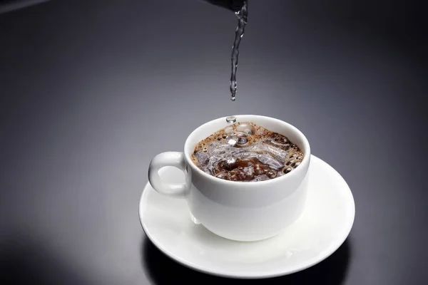 Przegotowanej wody przelewa się do białego kubka z czarnej kawy — Zdjęcie stockowe