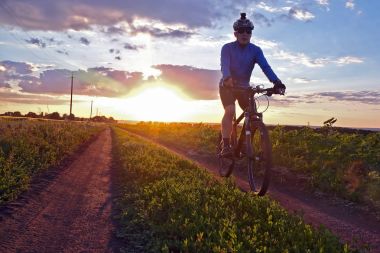 bisikletçi bir bisiklet ile günbatımında bir yolda gidiyor