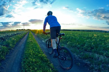 bisikletçi bir bisiklet ile günbatımında bir yolda gidiyor
