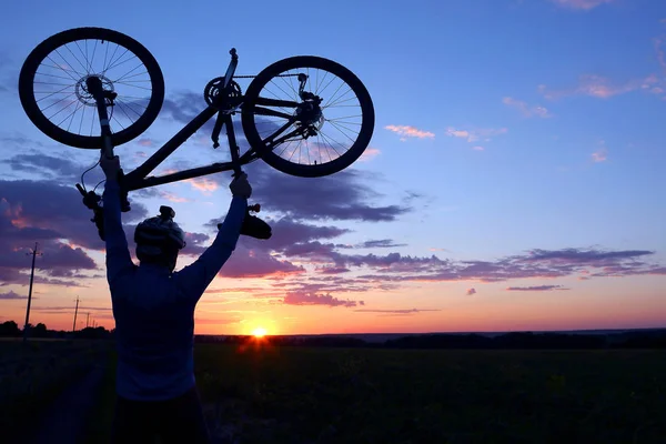 Bir bisikletçi bisiklet kadar günbatımında kaldırdı kollarını silüeti — Stok fotoğraf