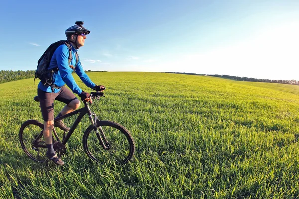 Radfahrer rast auf der grünen Wiese der Sonne entgegen — Stockfoto