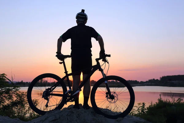 Silueta cyklista při pohledu na západ slunce na rybníku — Stock fotografie