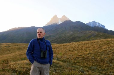 uzun yürüyüşe çıkan kimse dürbün ile dağlar bir arka plan üzerinde duruyor. Svaneti