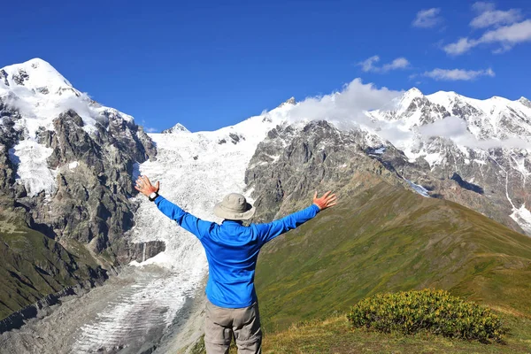 Человек с поднятыми руками стоит на фоне снежной горы — стоковое фото