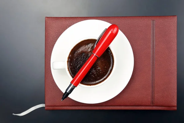 La penna rossa è sulla tazza con caffè nero e un notebook — Foto Stock