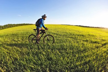 bisikletçi bir bisiklet ile yeşil alanda güneşin doğru gidiyor