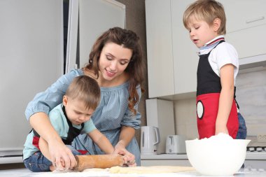 Anne genç oğulları mutfak masasının üzerinde hamur yoğurmak yardımcı olur.