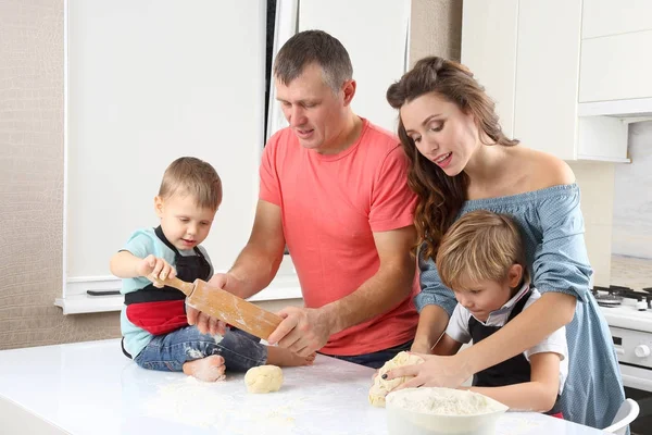 young parents help young sons knead the dough on the kitchen table