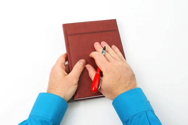 Manos sosteniendo un bolígrafo rojo y un cuaderno sobre fondo blanco — Foto de Stock