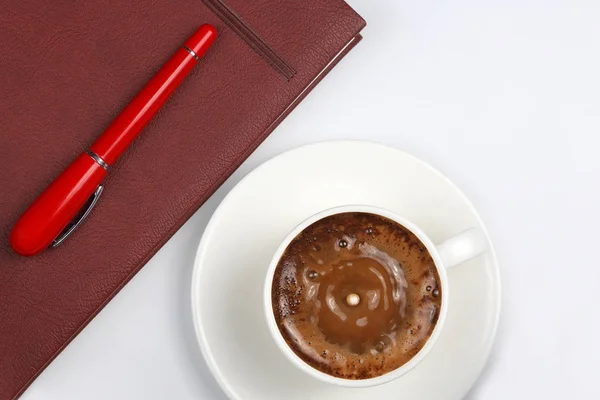 La pluma roja está en la taza con café negro y un cuaderno —  Fotos de Stock