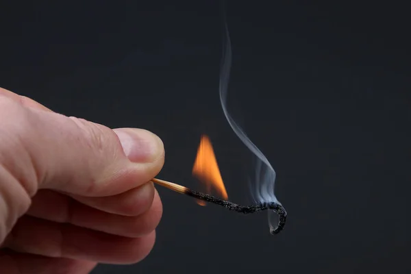 Горящая и курящая деревянная спичка в руке на темном заднем плане Стоковое Изображение