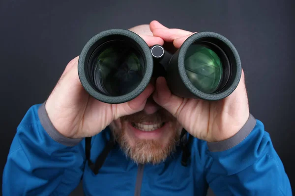 Hombre barbudo mirando a través de prismáticos sobre fondo gris —  Fotos de Stock
