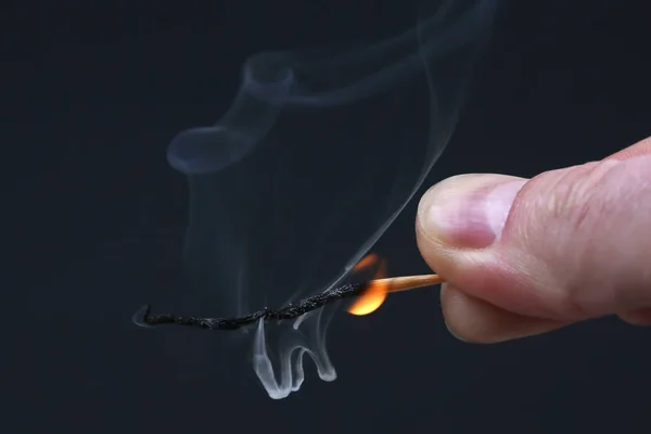 Spalování a kouření dřevěné zápas v ruce na tmavém pozadí — Stock fotografie