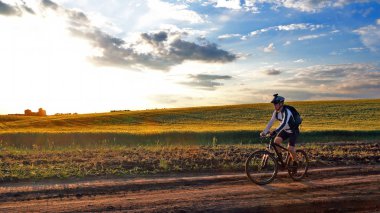 bisikletçi bir bisiklet ile günbatımında bir yolda gidiyor