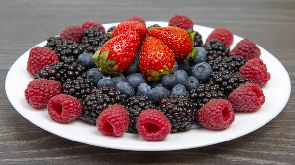 Moras, frambuesas y fresas en un plato blanco . — Foto de Stock