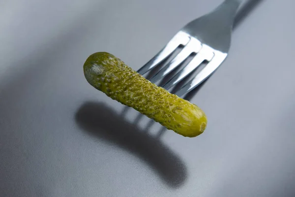 Pepino en escabeche en un tenedor en un primer plano de plato gris. comida y ve — Foto de Stock