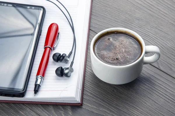 Taza de café negro, bolígrafo, teléfono móvil, portátil y auricular —  Fotos de Stock