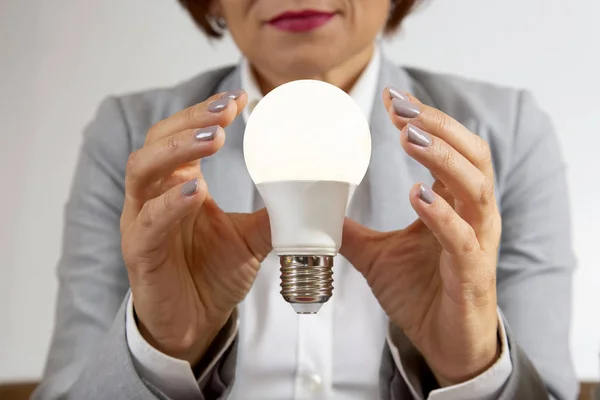 Mulher de negócios em um terno detém uma lâmpada elétrica ligada em seu — Fotografia de Stock